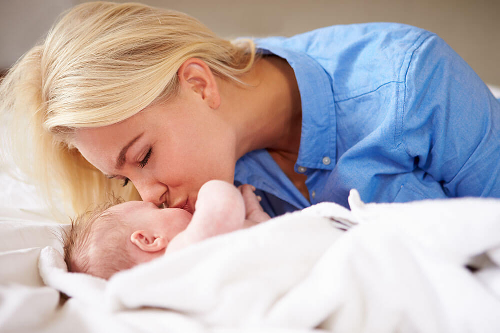 a mum kissing her newborn baby