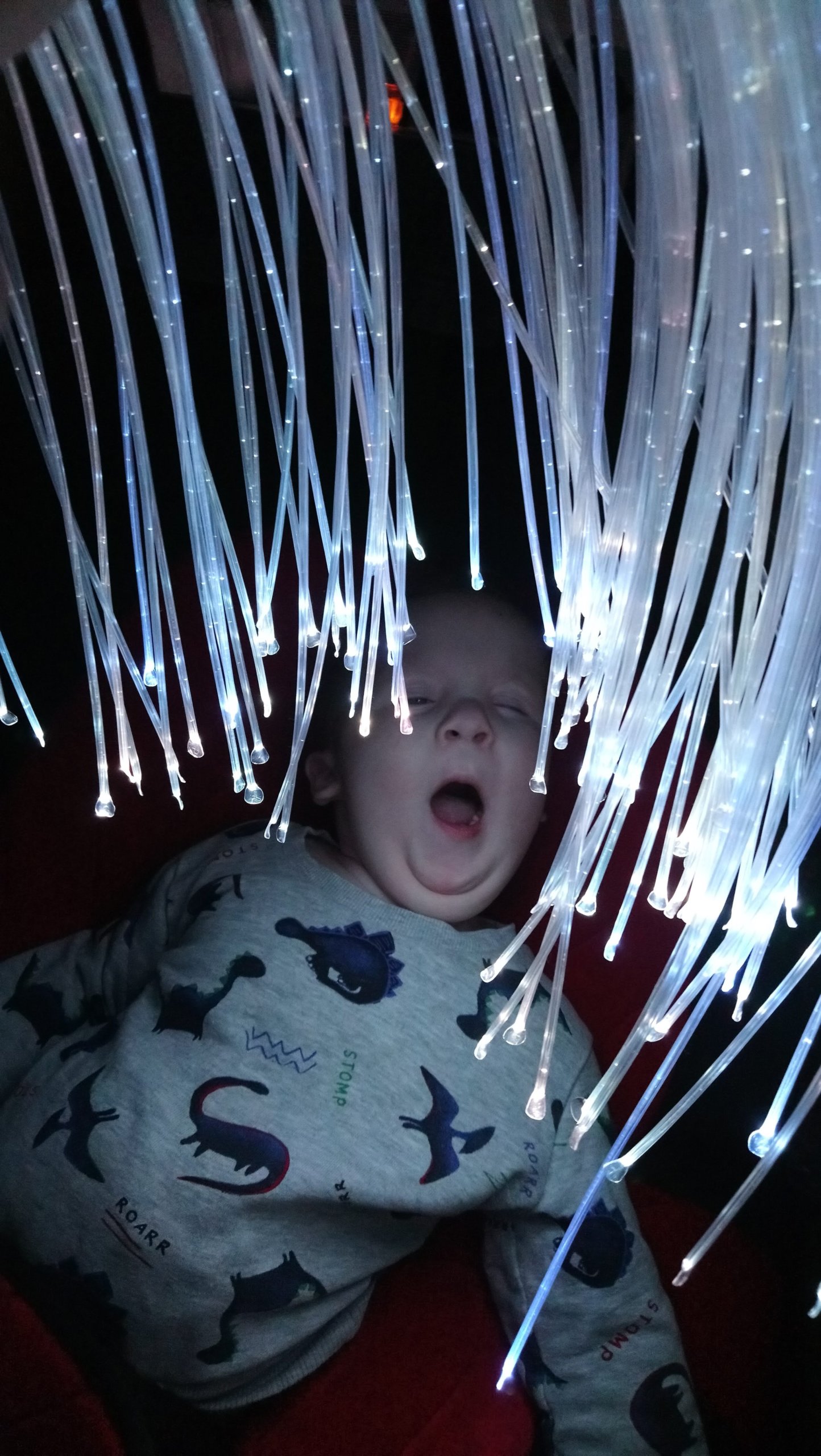 Evan yawning while looking at white fibre optic lights