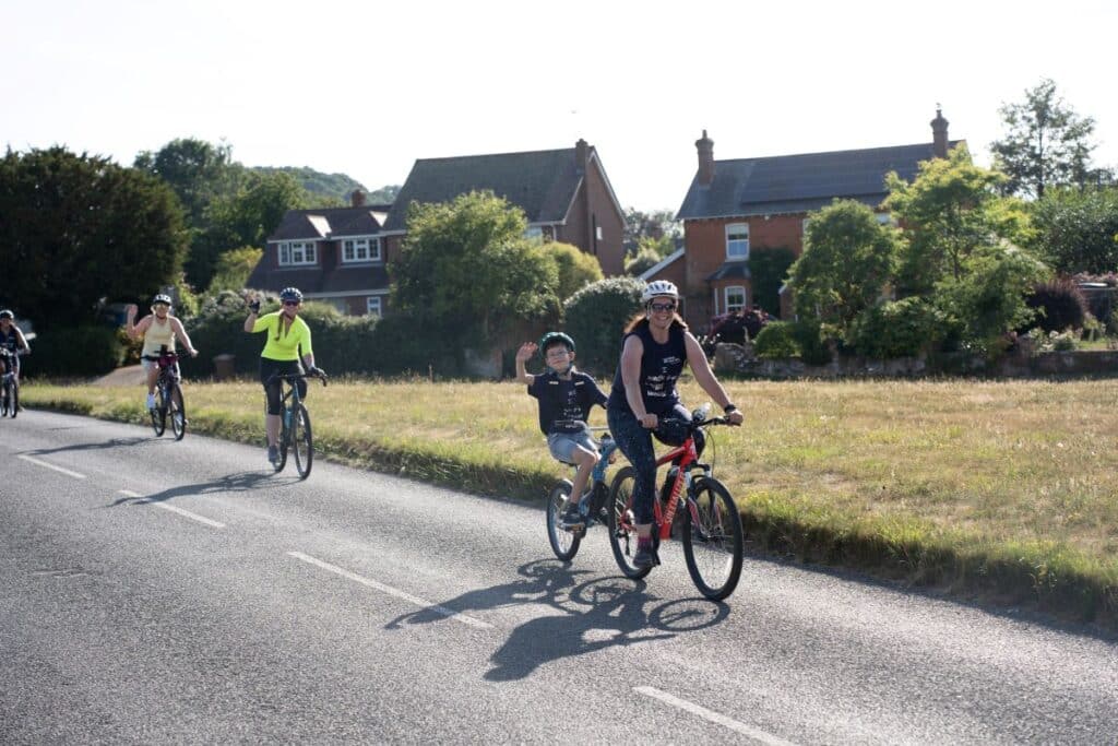 Mother and son on tandem bike leading 3 other cyclists down a road with houses in the background