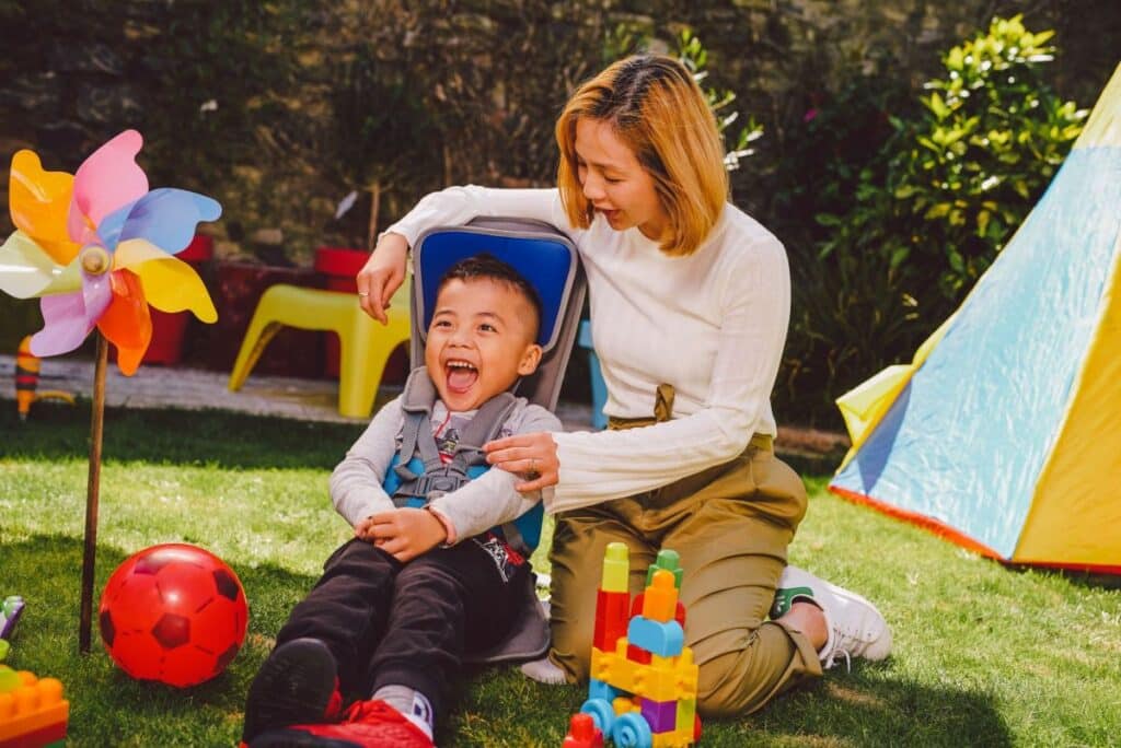 Child, smiling in a go to seat with mother watching him and toys around