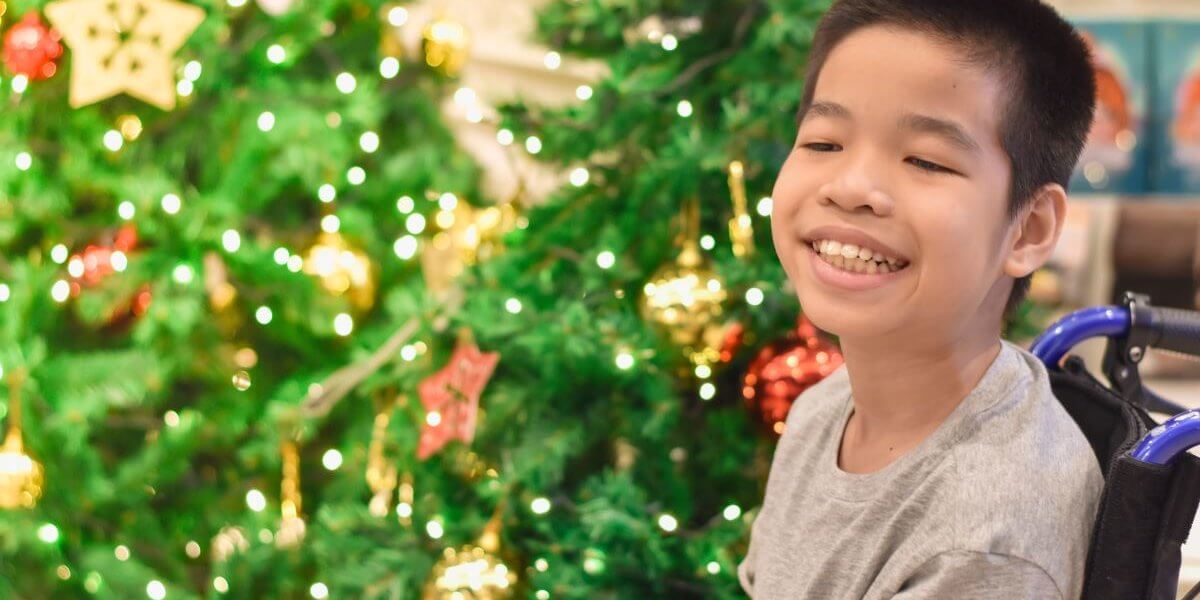a smiling boy in a wheelchair in front of a christmas