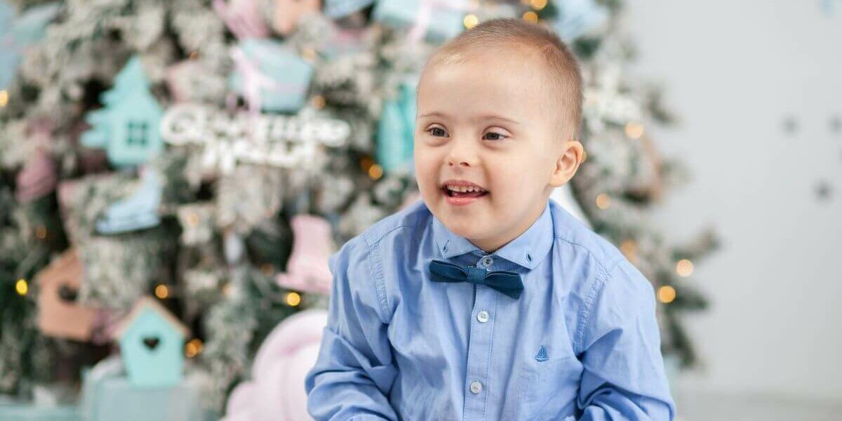 a little boy sat in front of a snowy christmas tree