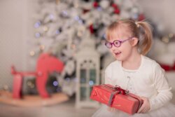 little girl in front of a christmas tree, holding a present