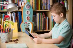 a young boy sat at a desk looking at an iPad
